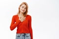 Enthusiastic young woman holds hand on heart, looks hopeful and happy at camera, stands over white background