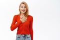 Enthusiastic young woman holds hand on heart, looks hopeful and happy at camera, stands over white background