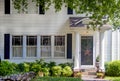 Entrance of charming white wood house with columns on porch and beautiful landscaping and overhanging branches and a red white and Royalty Free Stock Photo