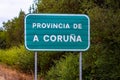 Entrance road sign of province of A Coruna on green background by dense trees in Spain