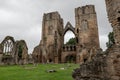 The entrance, ruin of main wall and courtyard of Elgin Cathedral with tourists in Scottish cloudy weather