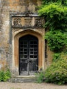 Entrance to a historic manor, framed by antique architectural elements and flanked by potted topiaries, features an aged door