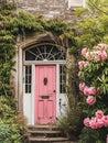 Entrance to a historic manor, framed by antique architectural elements and flanked by potted topiaries, features an aged door