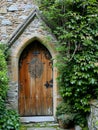 Entrance to a historic manor, framed by antique architectural elements and flanked by potted topiaries, features an aged door