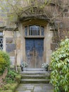 Entrance to a historic manor, framed by antique architectural elements and flanked by potted topiaries, features an aged door