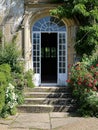 Entrance to a historic manor, framed by antique architectural elements and flanked by potted topiaries, features an aged door