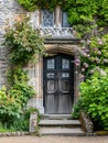 Entrance to a historic manor, framed by antique architectural elements and flanked by potted topiaries, features an aged door