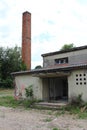 Entrance to old military barrack with broken windows and missing doors next to tall red brick chimney at abandoned military