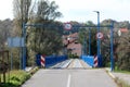 Entrance to partially renovated wavey old wooden bridge with new blue metal frame on each side and strong support with LED street