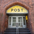 Entrance to the Post office in an historic building with a yellow sign, an old door and an arch of brick architecture in the old Royalty Free Stock Photo