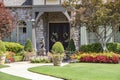 Entrance to upscale rock house with beautiful landscaping and a statue and wreaths and benches beside front porch Royalty Free Stock Photo