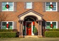 Entrance of two story brick house with arched porch decorated for Christmas with wreaths on windows and garland with red ribbons Royalty Free Stock Photo