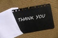 An envelope and black paper written with Thank You on a cork board