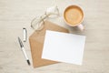 Envelope with blank paper card, cup of coffee, glasses and pen on white wooden table, flat lay Royalty Free Stock Photo