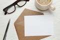 Envelope with blank paper card, cup of coffee, pen and glasses on white wooden table, flat lay Royalty Free Stock Photo