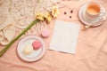 Envelope, flowers, and macarons with cup of tea on light background