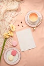 Envelope, flowers, and macarons with cup of tea on light background