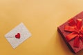 Envelope with a symbol in the form of a red heart and next box with a gift bandaged with a ribbon on a yellow background Royalty Free Stock Photo