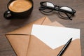 Envelopes with blank paper card, cup of coffee, glasses and pen on wooden table, closeup Royalty Free Stock Photo