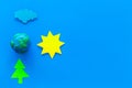 Environment protection concept. Plastiline symbol of planet Earth and sun, cloud, tree coutout on blue background top