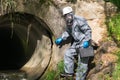 An environmental laboratory specialist in a protective suit and mask holds a case with a mobile laboratory in his hands and goes