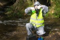 An environmental laboratory specialist in a protective suit and mask pours a sample of water from a test tube into a flask with