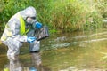 An environmental laboratory specialist in a protective suit and mask stands in the water and measures the level of pollution with