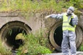 Environmental laboratory specialist in protective suit and mask talking on the phone and pointing at emergency site