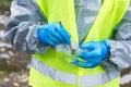 Environmental laboratory specialist in protective suit took a soil sample with tweezers and put a piece in a glass container,