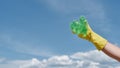 Environmental problems. Volunteers hand in yellow rubbish glove holding used plastic bottle against blue sky