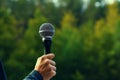 Environmental voice Hand holds microphone against green forest backdrop