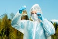 environmentalist in protective clothing and respirator examines the composition of the water from the lake