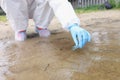 Environmentalist in protective suit and gloves taking water samples from lake closeup