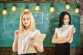 Envy and competition concept. Girl jealous of success of classmate in classroom, chalkboard on background. Woman with Royalty Free Stock Photo