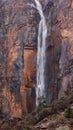 Ephemeral waterfall flowing over red and black sandstone cliffs in Zion Utah, USA