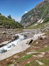 An epic Indian Himalayan Mountain valley with scenic water stream flowing through rocks and glaciers. Pony porter carrying Hikers