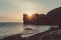 An epic sunset on the sea - the sun sets behind the mountain and everything shines with warm light with long rays.