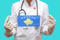 Epidemic in Kosovo. Young woman doctor in a medical coat and gloves holds a medical mask with the print of the flag of Kosovo on a