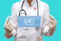 Epidemic in world. Young woman doctor in a medical coat and gloves holds a medical mask with the print of the flag of United