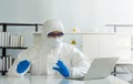 Epidemiological researchers in virus protective clothing look at laptop computer screen while holding Inoculating Needle and