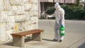 Epidemiologist in a hazmat suit sanitizes a public bench in a quarantined city Royalty Free Stock Photo