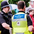 Police Officer And Rail Enforcement Officer Standing Talking Outside Railway Station