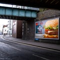 Railway Bridge Crossing A Main Road With A McDonalds Food Advertisment Poster With No People