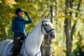 Equestrian lady riding white horseback in autumn alley