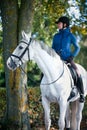 Equestrian lady riding white horseback in autumn alley