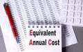 EQUIVALENT ANNUAL COST text on notebook with pen, calculator and chart on grey background