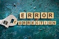 Error correction, word written on wooden blocks, adjustable wrench on cracked blue background. Error correction concept