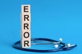ERROR word written on wooden blocks and stethoscope on light blue background