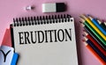 ERUDITION - a word written in a notebook on a pink background and colored pencils