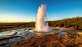 Eruption of a geyser surrounded by a forest under a bright blue sky during sunset Royalty Free Stock Photo